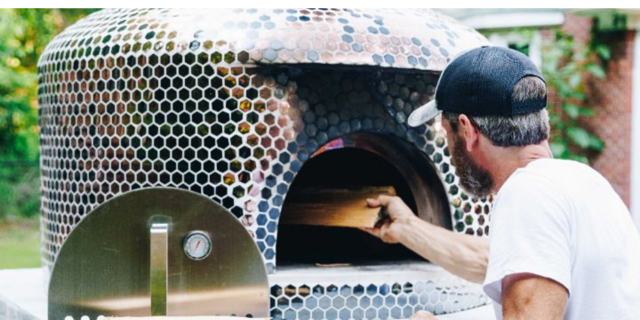 A farmer bakes a kosher organic pizza in a wood-fired oven outdoors on a farm at 10675 Chatsworth Hwy, Ellijay, Georgia 30540, surrounded by nature.