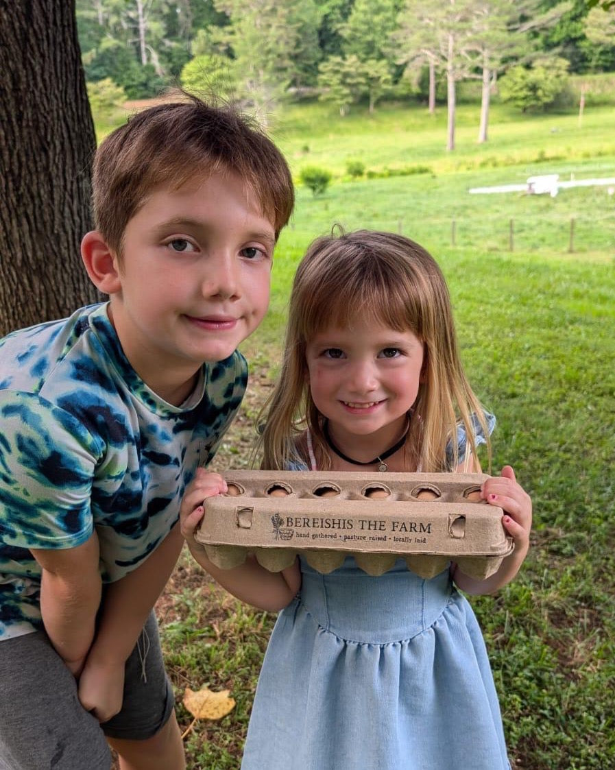 Two children holding a dozen kosher eggs on Bereishis The Farm, an organic farm in Ellijay, Georgia, offering yurt stays, animal visits, and farm tours.