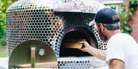 A farmer preparing kosher organic pizza in a wooden pizza oven outdoors at Bereishis The Farm, located on Chatsworth Hwy in Ellijay, Georgia.